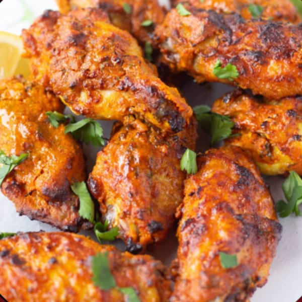 Close-up of Masala Slice's Indian-style chicken wings, garnished with fresh cilantro and a lemon wedge.