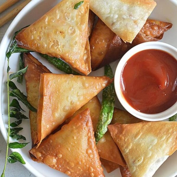 Crispy golden-brown samosas, garnished with green chilies and curry leaves, served with ketchup.